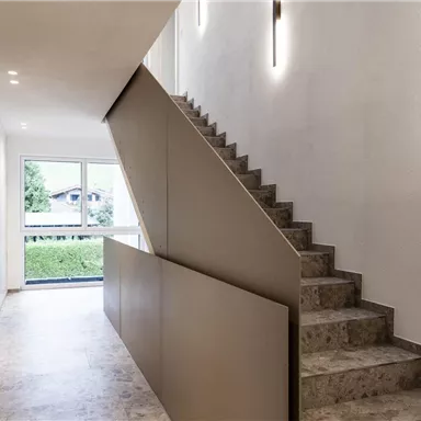 Ein moderner Eingangsbereich mit einer eleganten Treppe. Die Wände sind hell und mit sanften Lichtakzenten gestaltet.