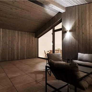 Ein moderner Innenraum mit Holzwänden und einer gemütlichen Sitzgelegenheit. Das Licht sorgt für eine warme, einladende Atmosphäre.