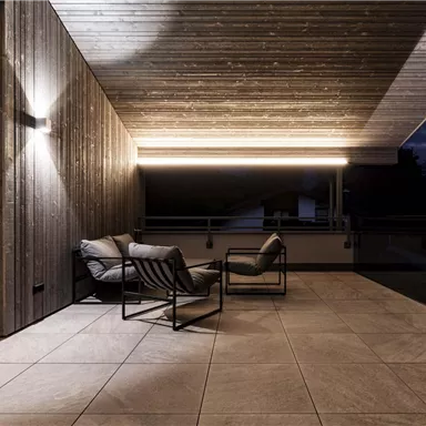 Eine moderne Terrasse mit stilvollen Sesseln und einer Holzverkleidung. Die sanfte Beleuchtung schafft eine gemütliche Atmosphäre in der Abenddämmerung.