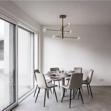 Ein modernes Esszimmer mit einem runden Tisch und eleganten Stühlen. Große Fenster lassen viel Licht herein und bieten einen Blick nach draußen.