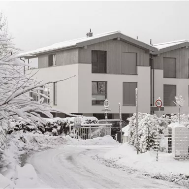 Ein modernes Haus im Schnee mit einem gewundenen Weg. Die Umgebung ist von einer winterlichen Landschaft geprägt, die Ruhe ausstrahlt.