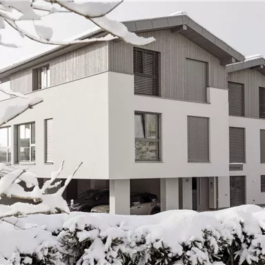 Ein modernes Haus im Winter, umgeben von Schnee. Die Architektur kombiniert Holz und Weiß und wirkt gleichzeitig gemütlich und stilvoll.