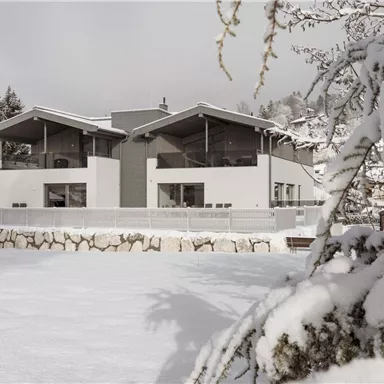 Ein modernes Haus im Schnee mit großen Fenstern und einem klaren Design. Umgeben von schneebedeckten Bäumen und einer ruhigen Winterlandschaft.