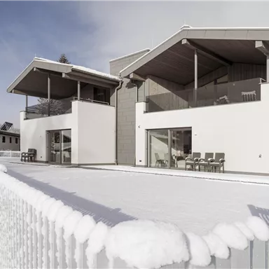 Ein modernes Haus mit Schnee bedeckt. Es hat große Fenster und einen gemütlichen Balkon.