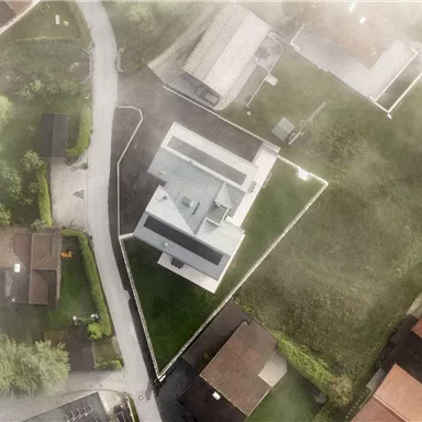 Ein modernes Haus mit einem gepflegten Garten, umgeben von anderen Wohngebäuden. Die Aufnahme ist aus der Vogelperspektive und zeigt eine ruhige Nachbarschaft.