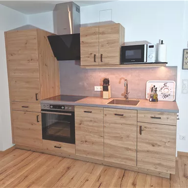 A modern kitchen made of wood with a countertop and a stove. It features a refrigerator and a microwave, as well as an elegant sink.