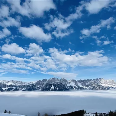 A breathtaking mountain landscape with snow-capped peaks and a deep blue sky. Fog covers the valley, lending a mystical atmosphere to the scene.