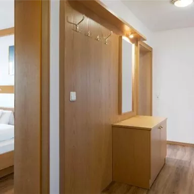 A bright and modern room with wooden decor. In the background, a double bed and a wardrobe can be seen.