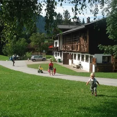 A picturesque landscape with a large green lawn and a traditional building. Children are playing and running happily along the path.