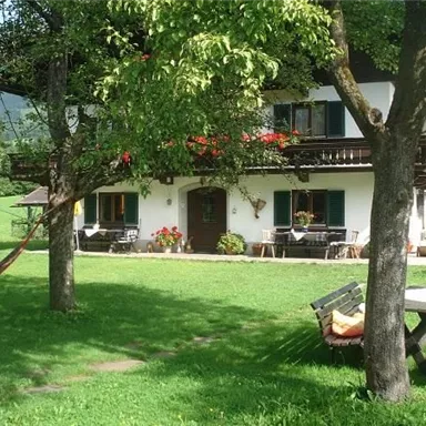 A beautiful house with a large garden and trees. The terrace is furnished with flowers and cozy furniture.