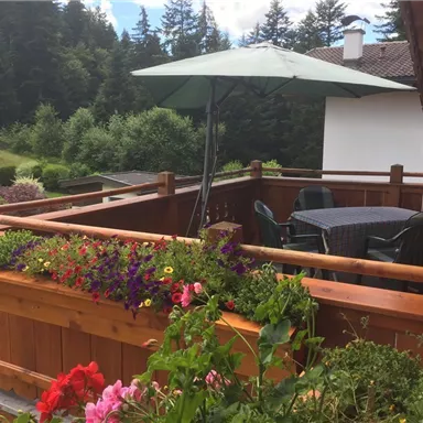 Ein gemütlicher Balkon mit einem großen Sonnenschirm und einem Tisch. Blumenrabatten bringen Farbe in die Umgebung.
