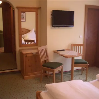A cozy hotel room with two beds, a table, chairs, and a television. In the background, an archway can be seen leading into another room.
