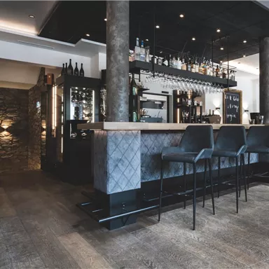Ein modernes Restaurant mit einer eleganten Bar und stilvollen Sitzgelegenheiten. Die Einrichtung ist hell und einladend, mit Holzfußboden und sanften Beleuchtungselementen.