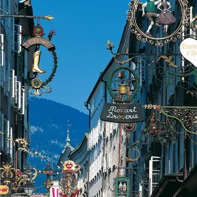 Eine belebte Straße mit historischen Schildern und Blick auf die Berge. Der Himmel ist klar und blau.