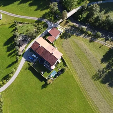 Ein Luftbild von einem ländlichen Gebiet mit mehreren Häusern und grünen Wiesen. Die Wege sind klar erkennbar und umgeben von Bäumen.