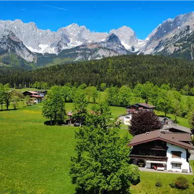 A picturesque landscape with green meadows and mountains in the background. Here are some buildings and trees that create a peaceful atmosphere.