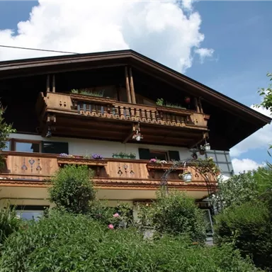 A traditional house with a large balcony and beautiful wooden decorations. Surrounded by lush greenery and a clear sky.