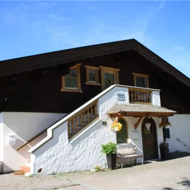 A charming house in traditional style with a wooden upper floor. The entrance area is welcoming, surrounded by green vegetation.