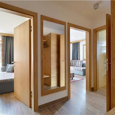 A bright hallway with open doors and modern furniture. A cozy living room and a mirror are visible.