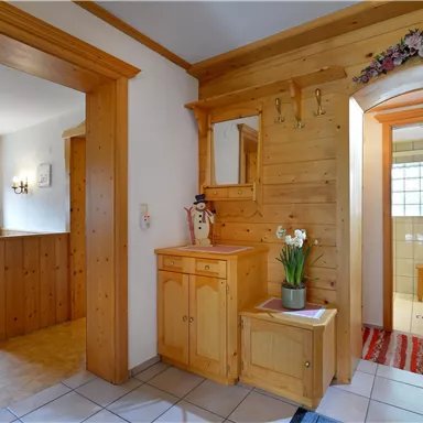 A cozy entrance area with wood-paneled walls and a small table with flowers. The room has a warm, inviting atmosphere.