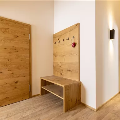 A bright hallway with a wooden door and a wooden bench. Coat hooks and a small heart decoration hang on the wall.