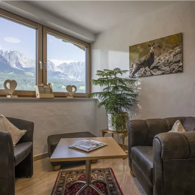 A cozy living space with two armchairs and a table. Large windows offer a view of the mountains.