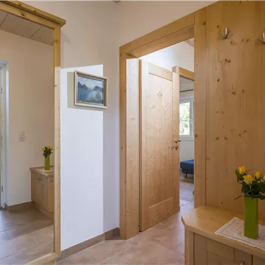 A bright hallway with wooden walls and doors. On a table stands a vase with yellow flowers.