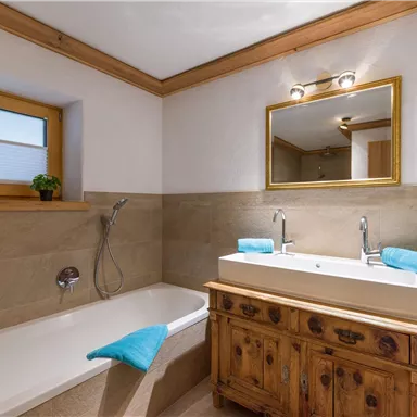 A modern bathroom with a bathtub and two sinks. Wood and stone surfaces create a warm atmosphere.