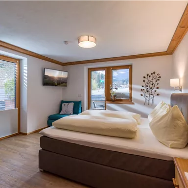 A cozy bedroom with a large bed and light wood decor. Windows let in plenty of daylight, and a comfortable couch complements the space.