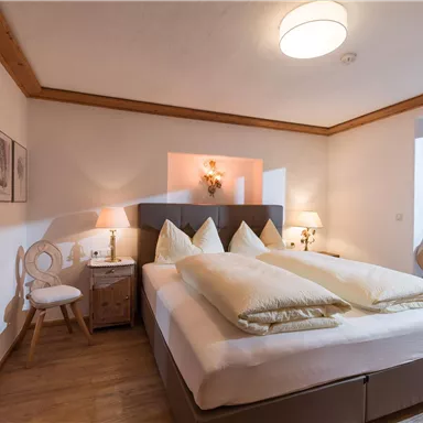 A cozy bedroom with a large double bed and bright pillows. The warm lighting and neutral colors create an inviting atmosphere.