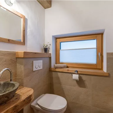 A modern bathroom with a stone wash basin and wooden shelves. The window brings daylight into the room and creates a pleasant atmosphere.