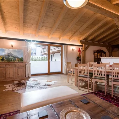 A bright living room with wood paneling and large windows. There is a dining area with a wooden table and chairs, as well as a cozy rug.