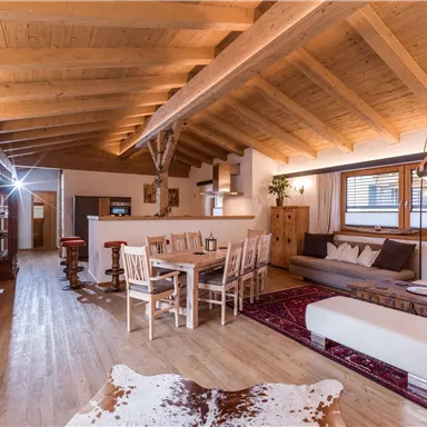 A modern living and dining room with a wooden beam ceiling. The space is bright and cozy, ideal for relaxation and social evenings.