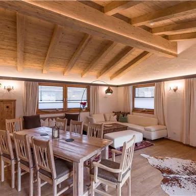 A cozy living room with a wooden ceiling and a large dining table. The windows let in plenty of light and the furniture is modern and inviting.