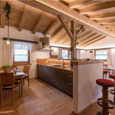 A modern kitchen with a wooden ceiling and a cozy dining area. The decor is friendly and bright, with large windows for plenty of natural light.