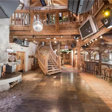 A cozy interior with rustic wood design and a spiral staircase. The bar is well-equipped, and the floor is made of tiles and stone.