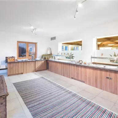 A modern breakfast buffet with wooden shelves and a spacious counter. Bright walls and natural lighting create a friendly atmosphere.