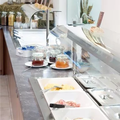 A buffet with various dishes, including eggs, ham, and jam. The dining table is designed to be bright and clean.
