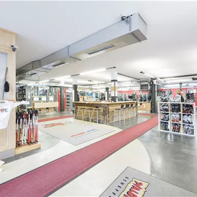 A modern sales area with sports goods and a bar. The walls are decorated with shelves and mirrors, while the floor is accented with red carpet.