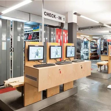A modern check-in area with multiple computer stations. In the background, shelves with sports equipment are visible.