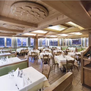 A cozy restaurant with wooden elements and several tables. The tables are covered with white tablecloths and the room is brightly lit.
