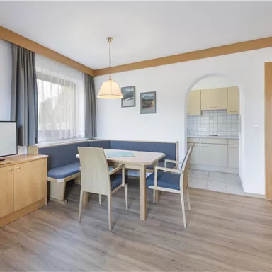 A cozy living space with a dining area and a television. The kitchen is visible through an archway and the floor is made of wood.