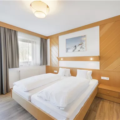 A bright bedroom with a large double bed and wooden decorations. Large windows provide plenty of daylight and a cozy atmosphere.