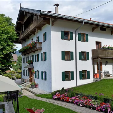 Ein charmantes, weißes Haus mit grünen Fensterläden und einem Balkon. Der Garten ist blühend und lädt zum Entspannen ein.