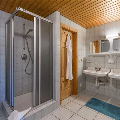 Ein modernes Badezimmer mit einer Dusche und zwei Waschbecken. Die Wände sind gefliest und es gibt einen Holzdeckenbelag.