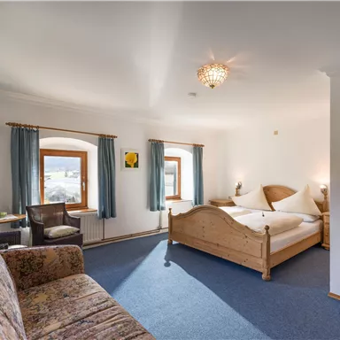 Ein komfortables Zimmer mit einem großen Bett und einer gemütlichen Sitzecke. Helle Fenster sorgen für eine freundliche Atmosphäre.