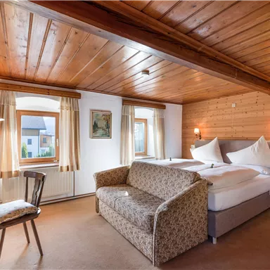 Ein gemütliches Zimmer mit Holzwänden und einem Doppelbett. Es gibt einen kleinen Tisch und einen Sofa-Bereich, ideal zum Entspannen.