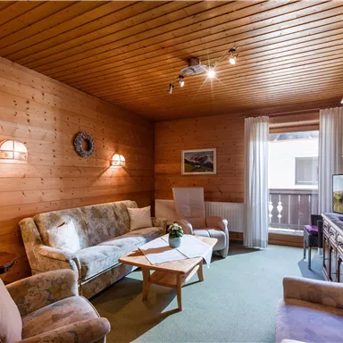 Ein gemütliches Wohnzimmer mit Holzwänden und einer warmen Beleuchtung. Es gibt bequeme Sofas und einen kleinen Tisch, ideal zum Entspannen.
