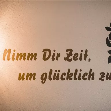 Eine Wand mit einem Zitat in deutscher Sprache und einer stilisierten Rose. Es erinnert daran, sich Zeit für das Glück zu nehmen.