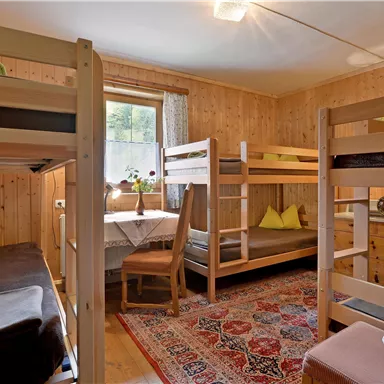 A cozy sleeping room with wooden bunk beds. The room is bright and friendly, with a table and chairs.